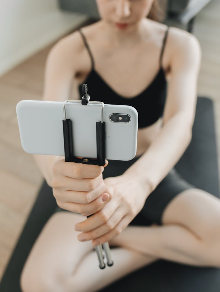 Woman holding smartphone on tripod during yoga session indoors.